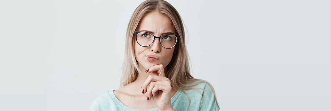 Een blonde vrouw met een bril raakt nadenkend haar kin aan